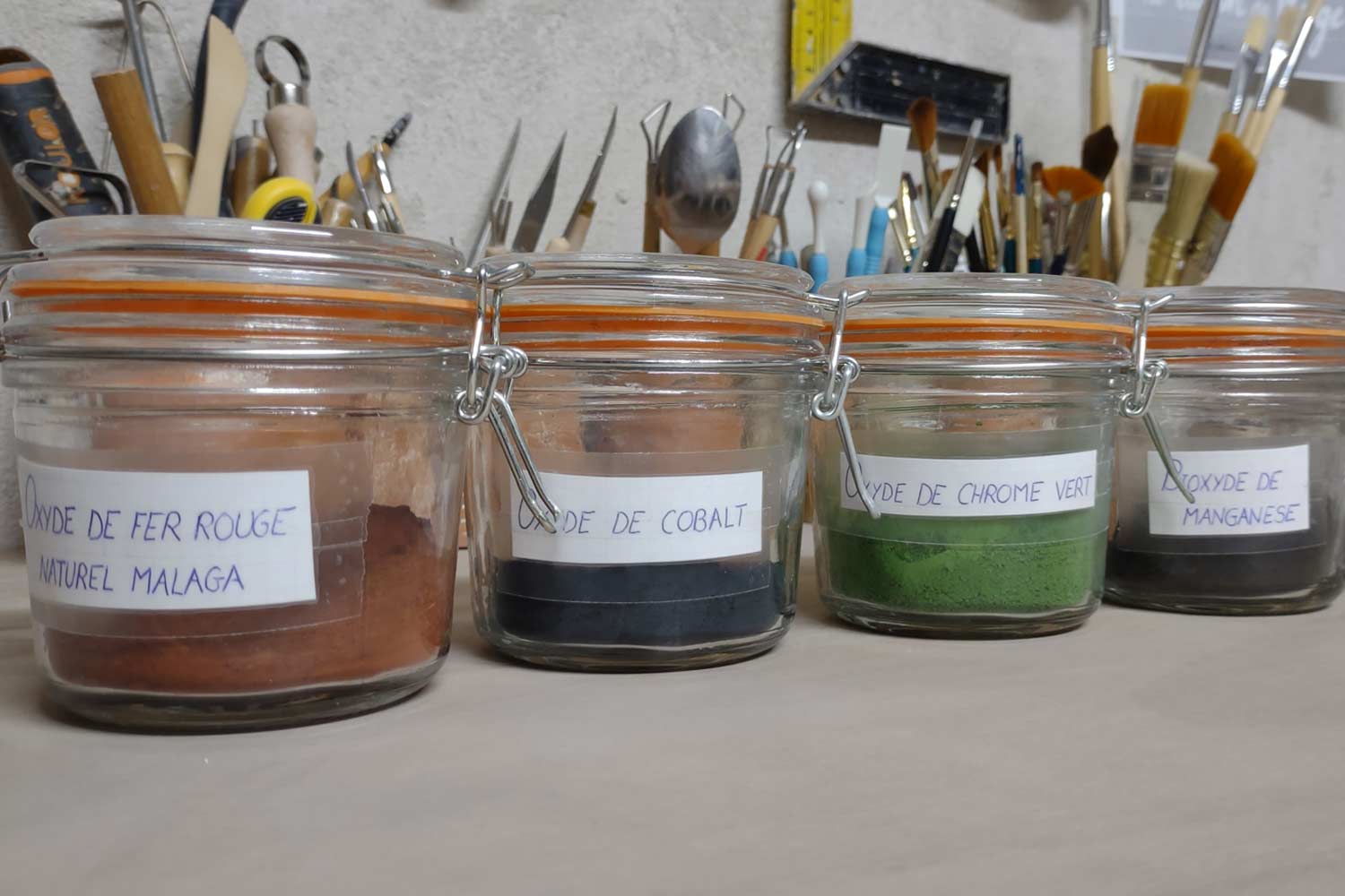 Plusieurs pots en verre contenant des oxydes servant à la fabrication d'engobes et d'émaux